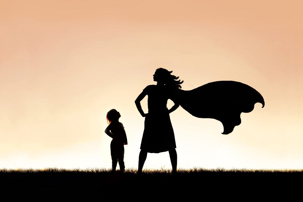 A mother standing strong wearing a superhero cape with her child looking up at her.